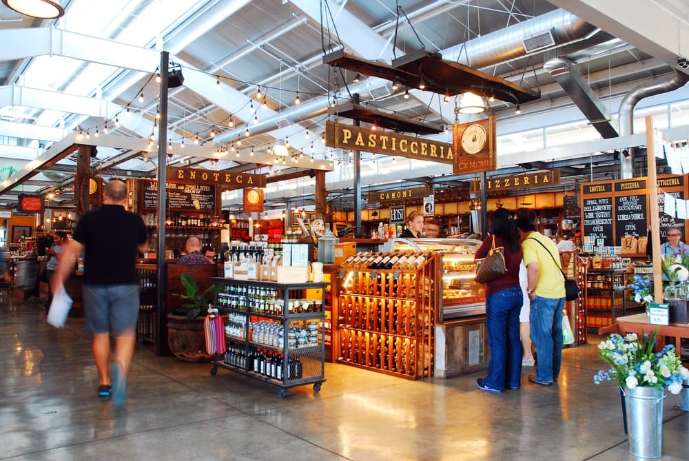 A bustling market interior with various food stalls and signage for pasticceria and enoteca.