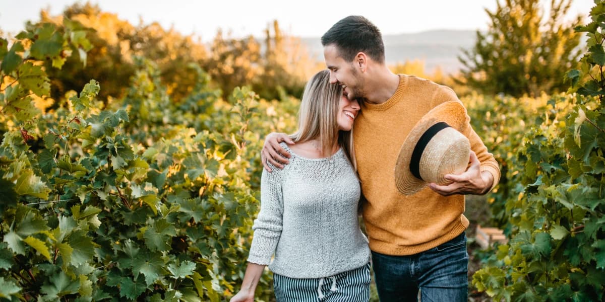 A couple embraces joyfully among vineyard rows during golden hour.
