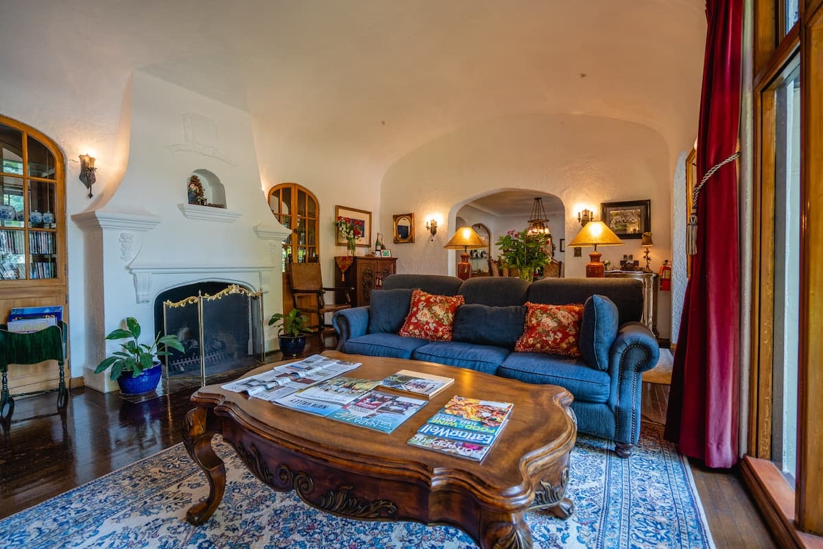 A cozy living room featuring a blue sofa with red pillows, a wooden coffee table with magazines, and a fireplace.