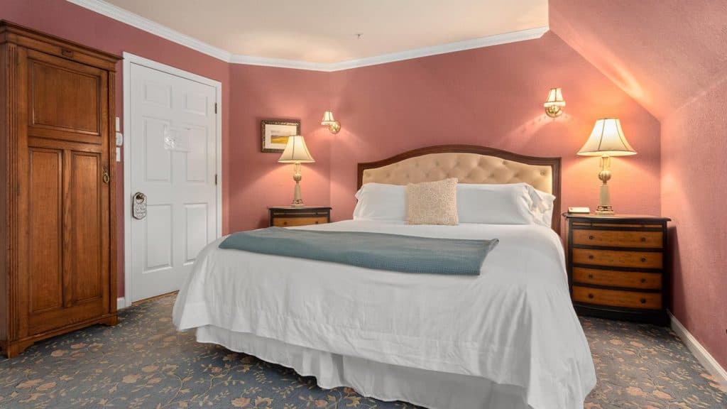 Cozy bedroom featuring a soft bed, bedside tables, lamps, and warm pink walls.