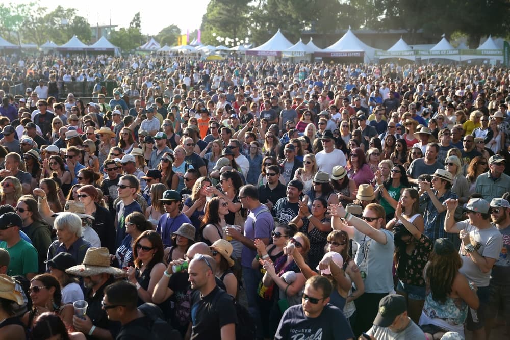 A large crowd of people enjoying a music festival under clear skies.