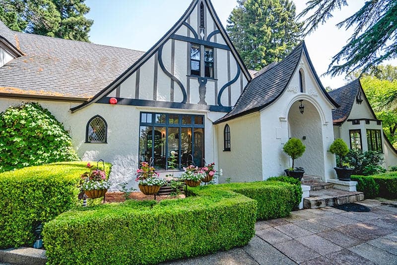 A charming Tudor-style house surrounded by well-manicured hedges and flower pots.