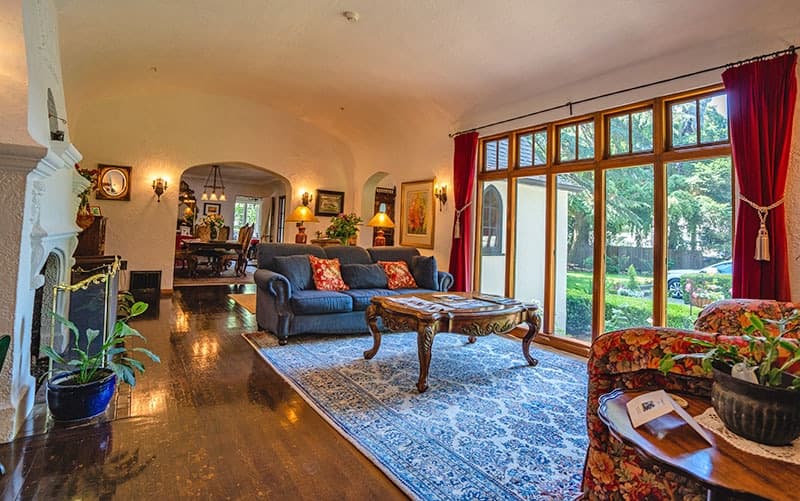 A cozy living room with a blue sofa, wooden coffee table, and large windows letting in natural light.