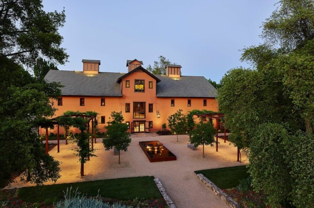 A modern, two-story orange house surrounded by landscaped gardens and trees.