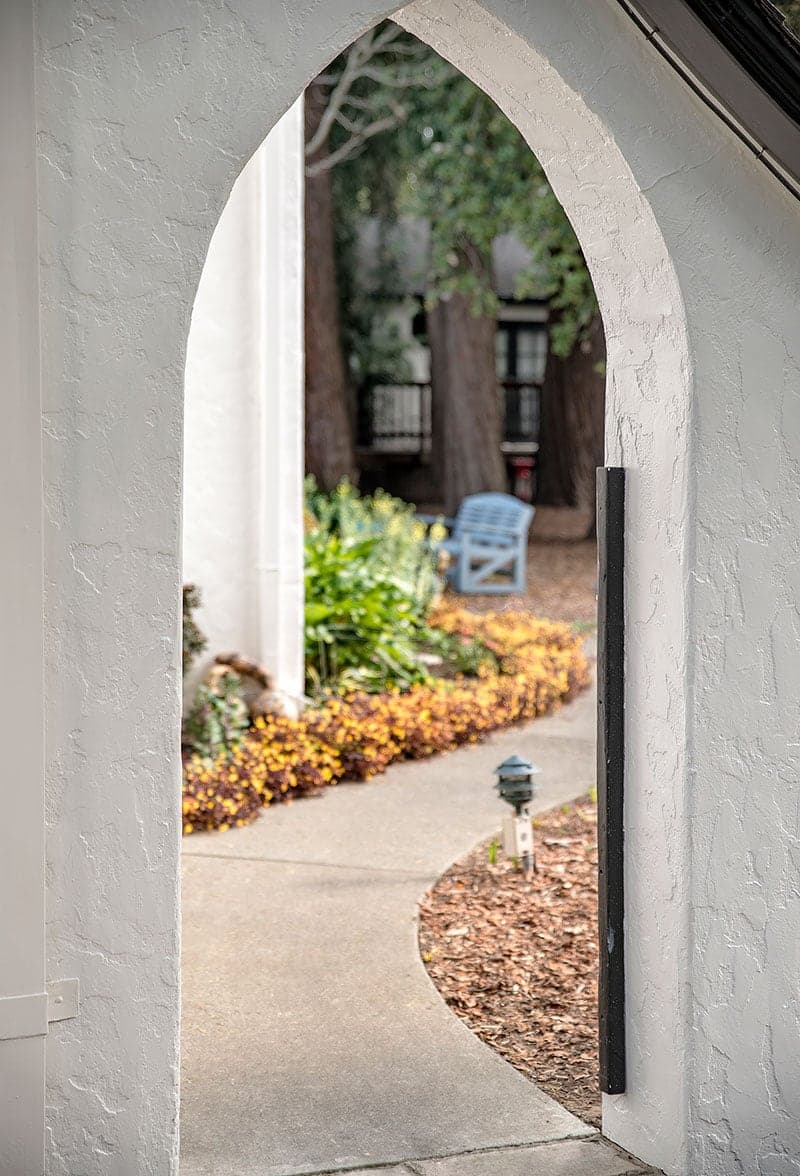 A view through an arched entrance leading to a pathway surrounded by colorful flowers and greenery.