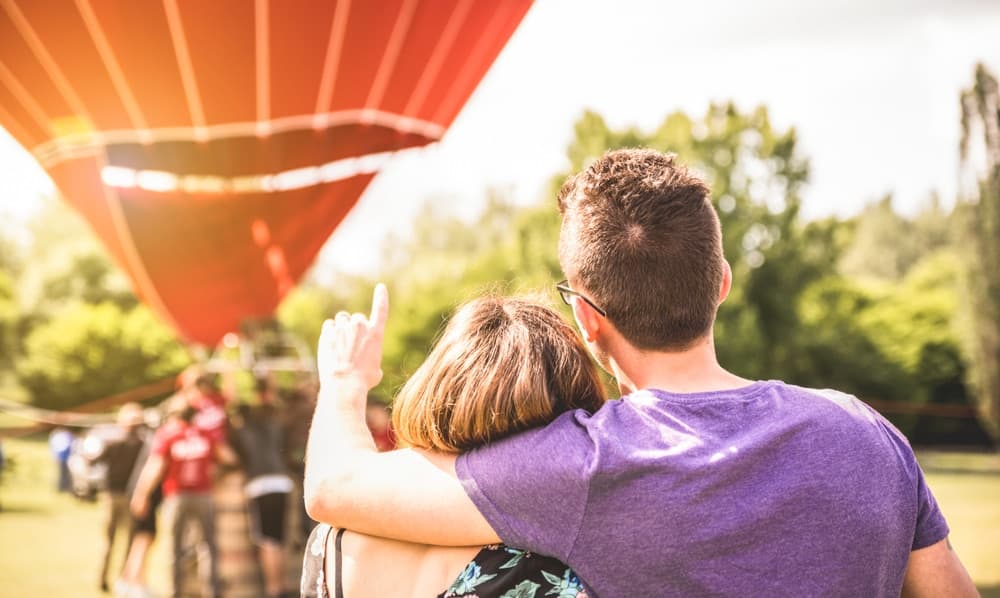 A couple embraces while watching a hot air balloon being prepared for flight in a field.