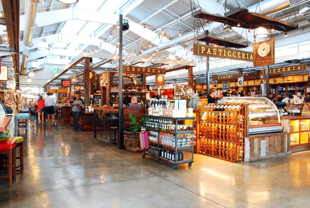 A bustling indoor market with various food stalls and shops under a bright, open ceiling.