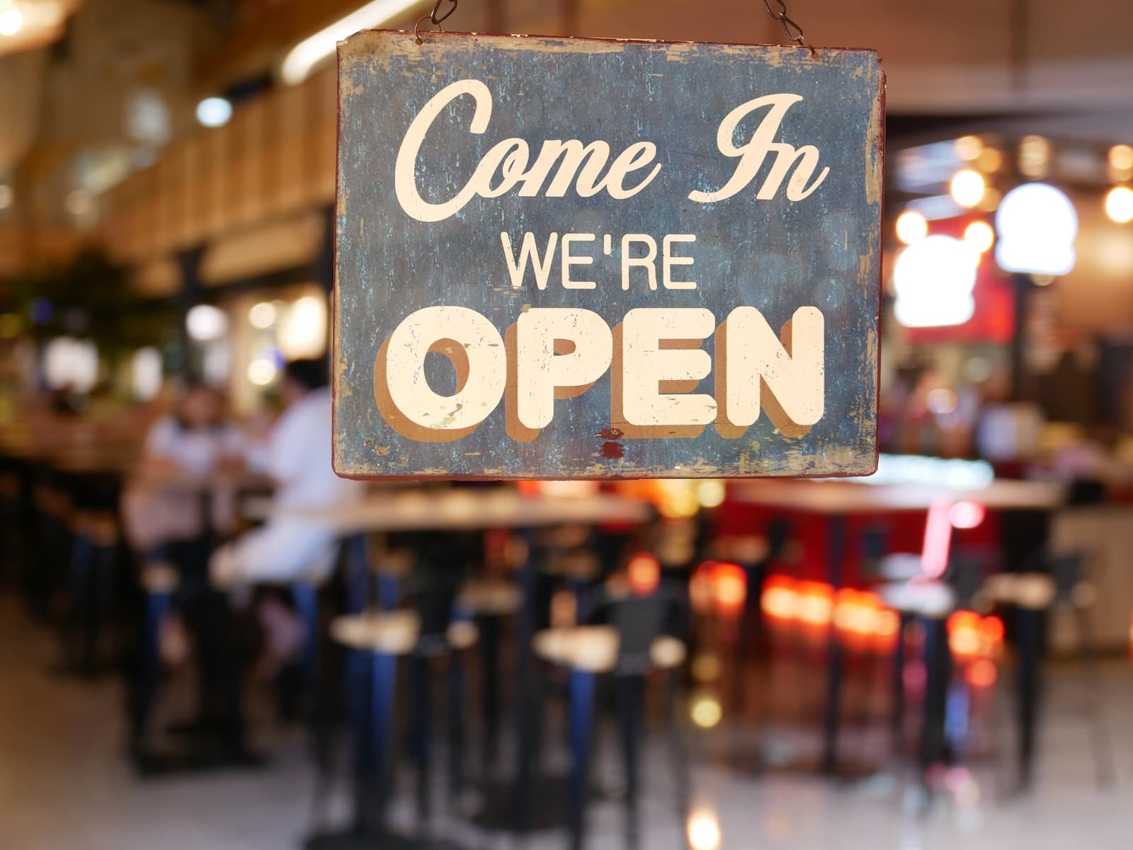 A rustic "Come In, We're Open" sign hangs in a bustling café.