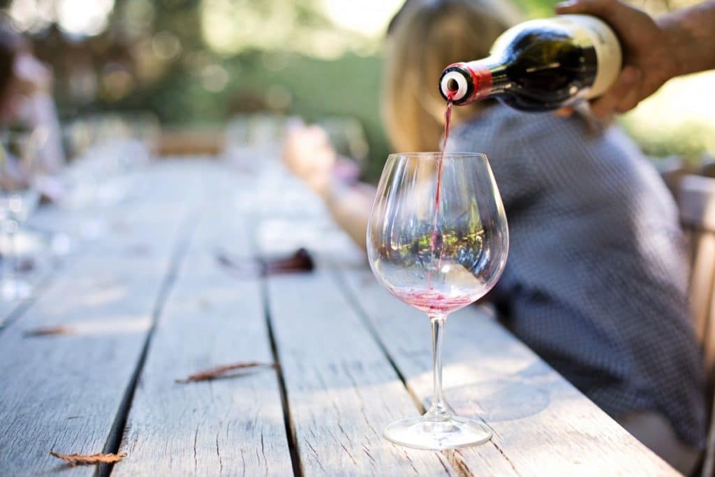 A hand pours red wine into a glass on a rustic wooden table.