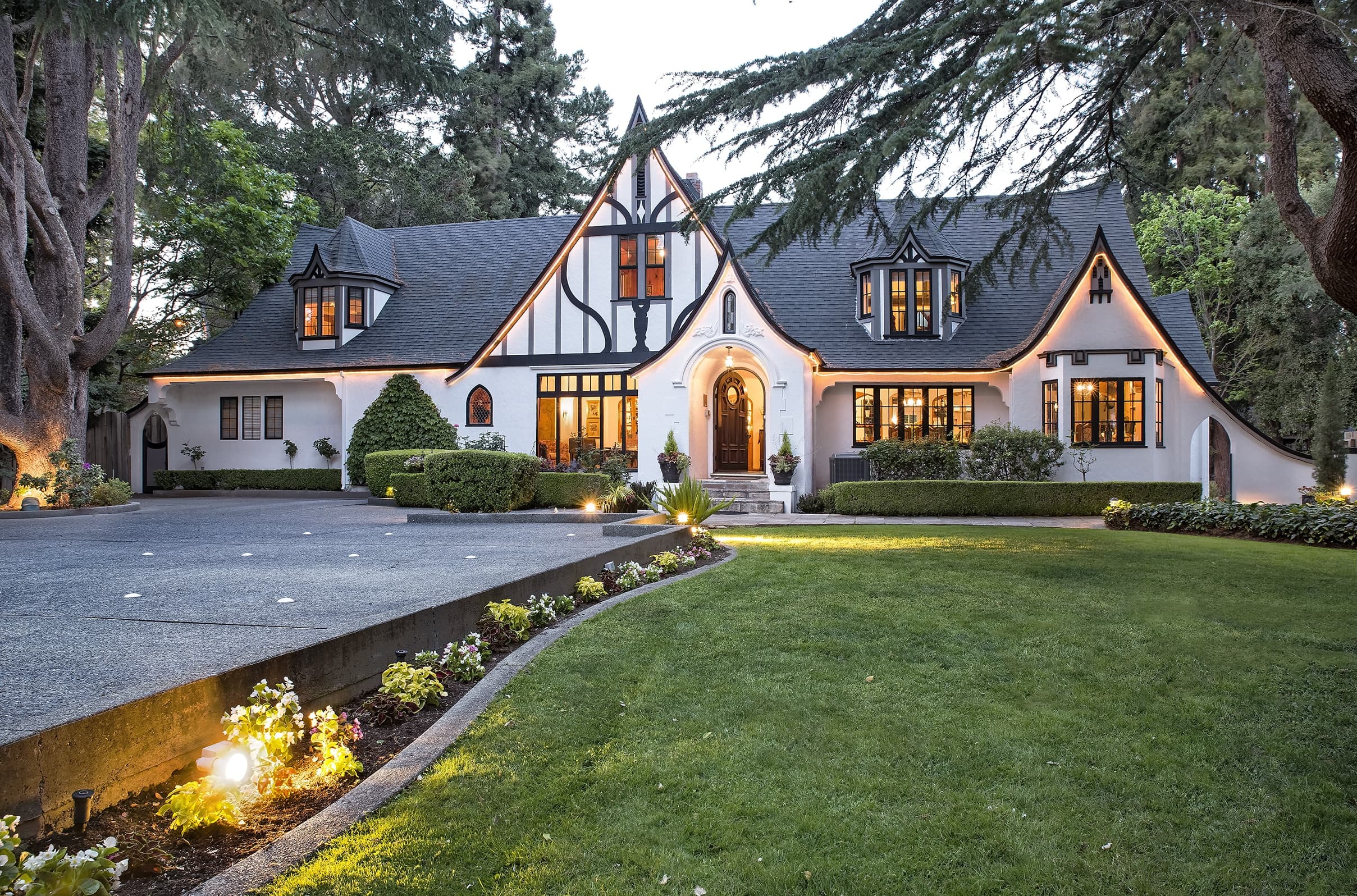 A charming Tudor-style home with a manicured lawn and warm exterior lighting.