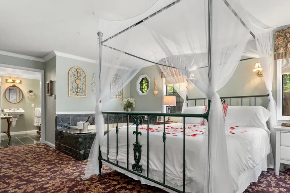 A cozy bedroom featuring a four-poster bed draped with sheer fabric, surrounded by elegant decor and a private bathroom.