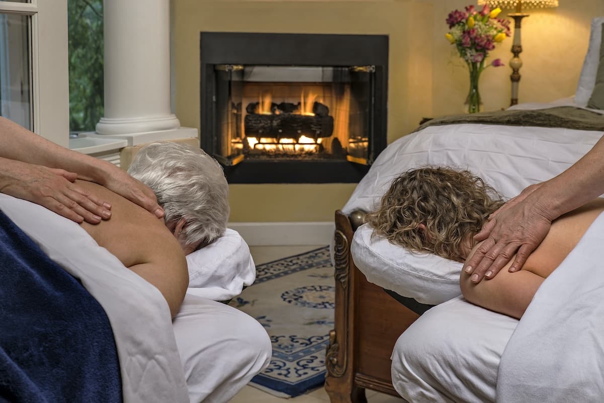 A cozy massage setting with two people receiving treatments by a fireplace.