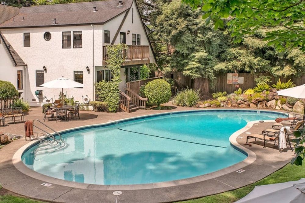 A backyard pool surrounded by lush greenery and seating areas next to a stylish house.