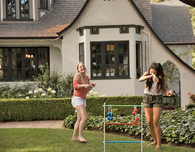 Two women play a game in a lush backyard near a charming house.