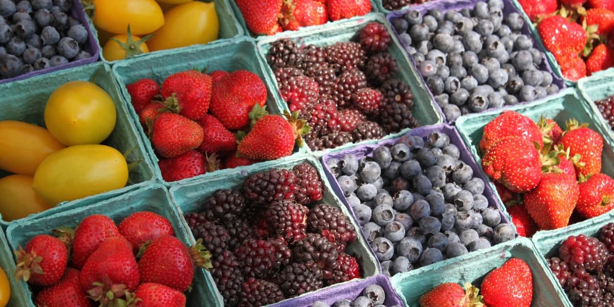 A colorful display of various fruits, including strawberries, blueberries, blackberries, and yellow plums in small containers.