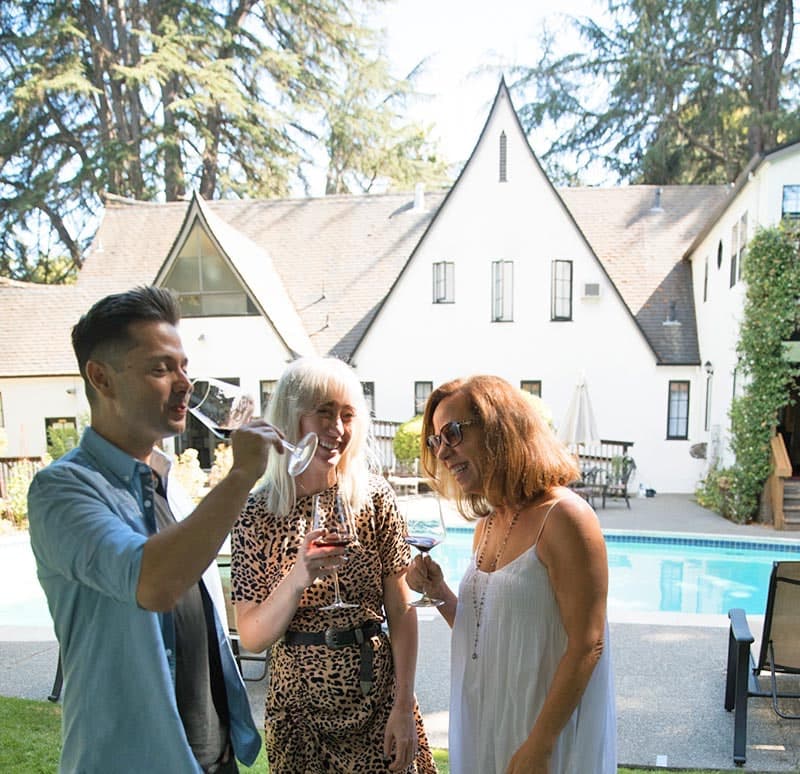 Three people enjoy drinks together by a poolside in a sunny setting.