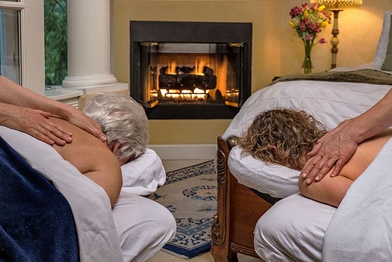 Two people receiving massages near a cozy fireplace.