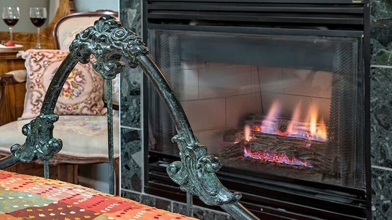 A decorative chair in front of a cozy fireplace with flickering flames.