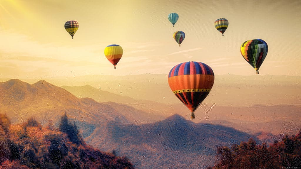 A scenic view of multiple colorful hot air balloons soaring over mountains at sunrise.