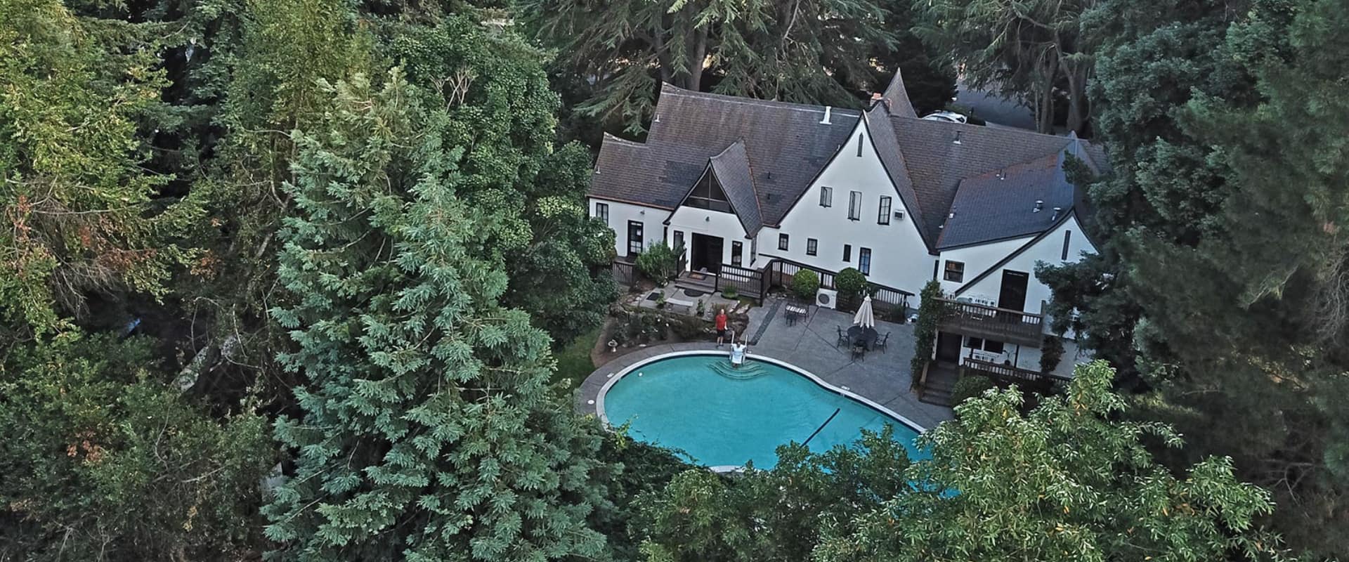 Aerial view of a large, modern house surrounded by dense trees and a swimming pool.