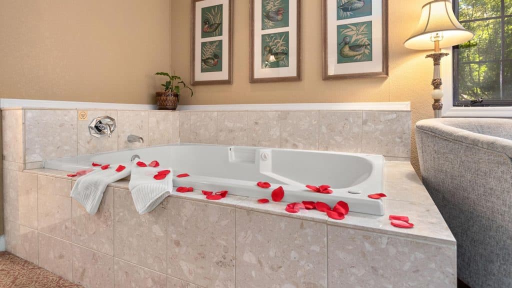 A luxurious jetted bathtub surrounded by rose petals in a cozy, well-decorated bathroom.