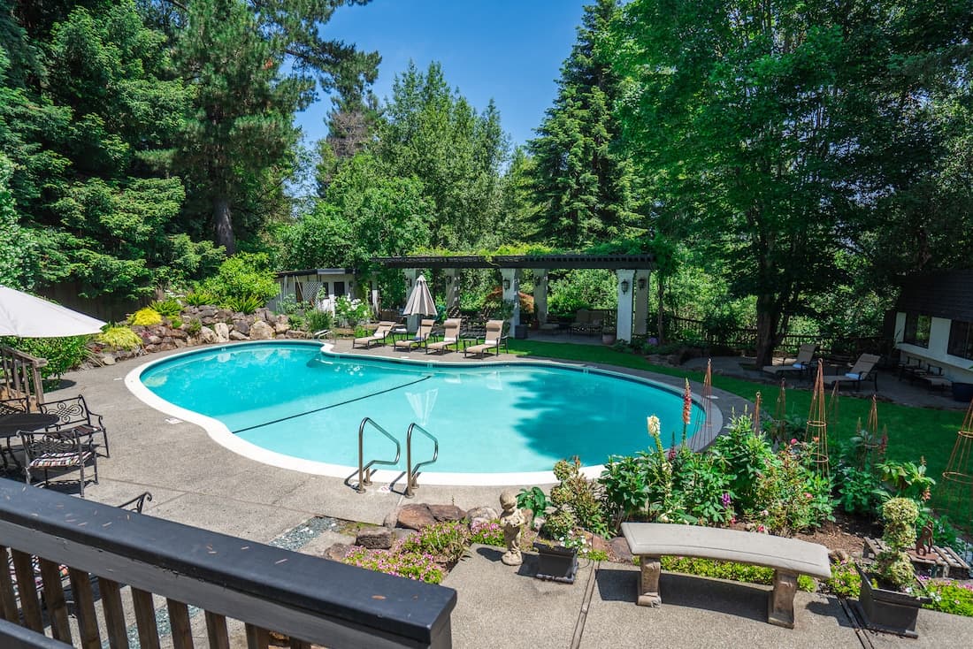 A tranquil backyard with a swimming pool surrounded by lush greenery and comfortable seating.