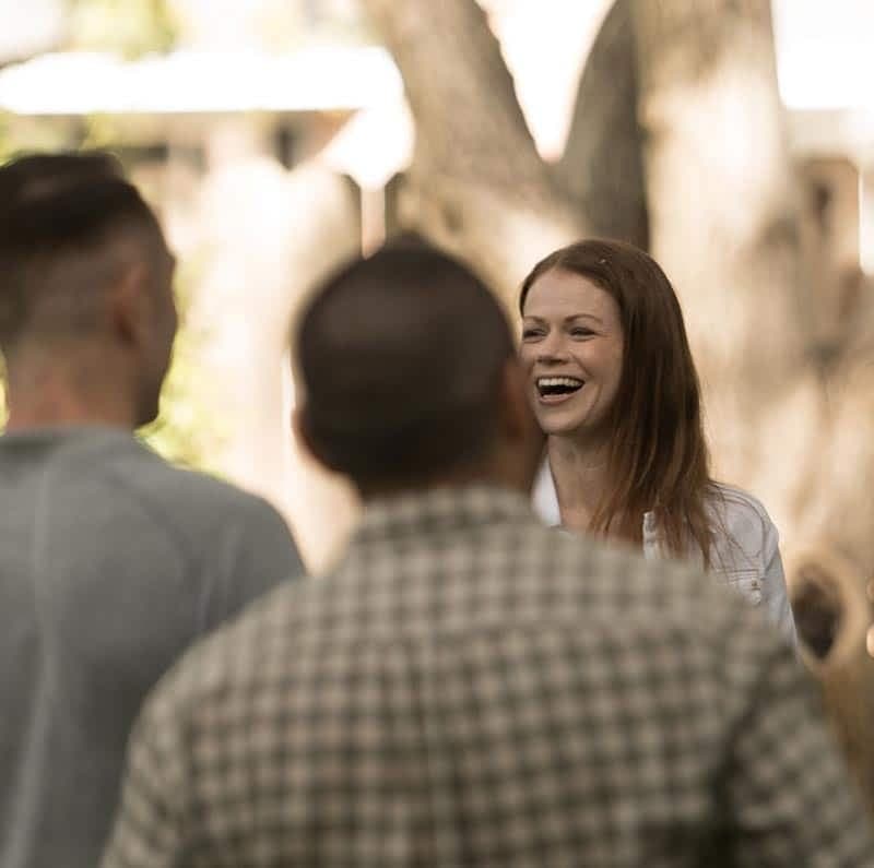 A smiling woman chats with two men outdoors.