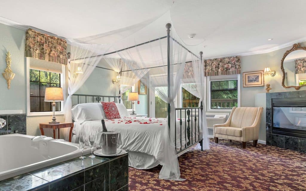 A cozy bedroom featuring a four-poster bed with sheer drapes, a jacuzzi tub, and stylish decor.
