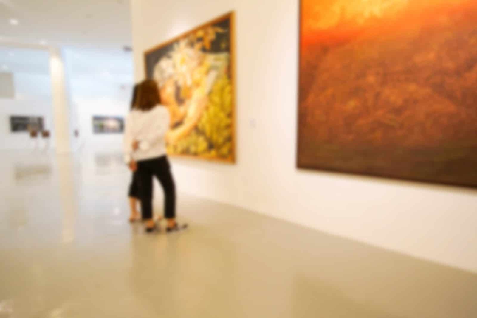 Two visitors admire paintings in a bright art gallery.