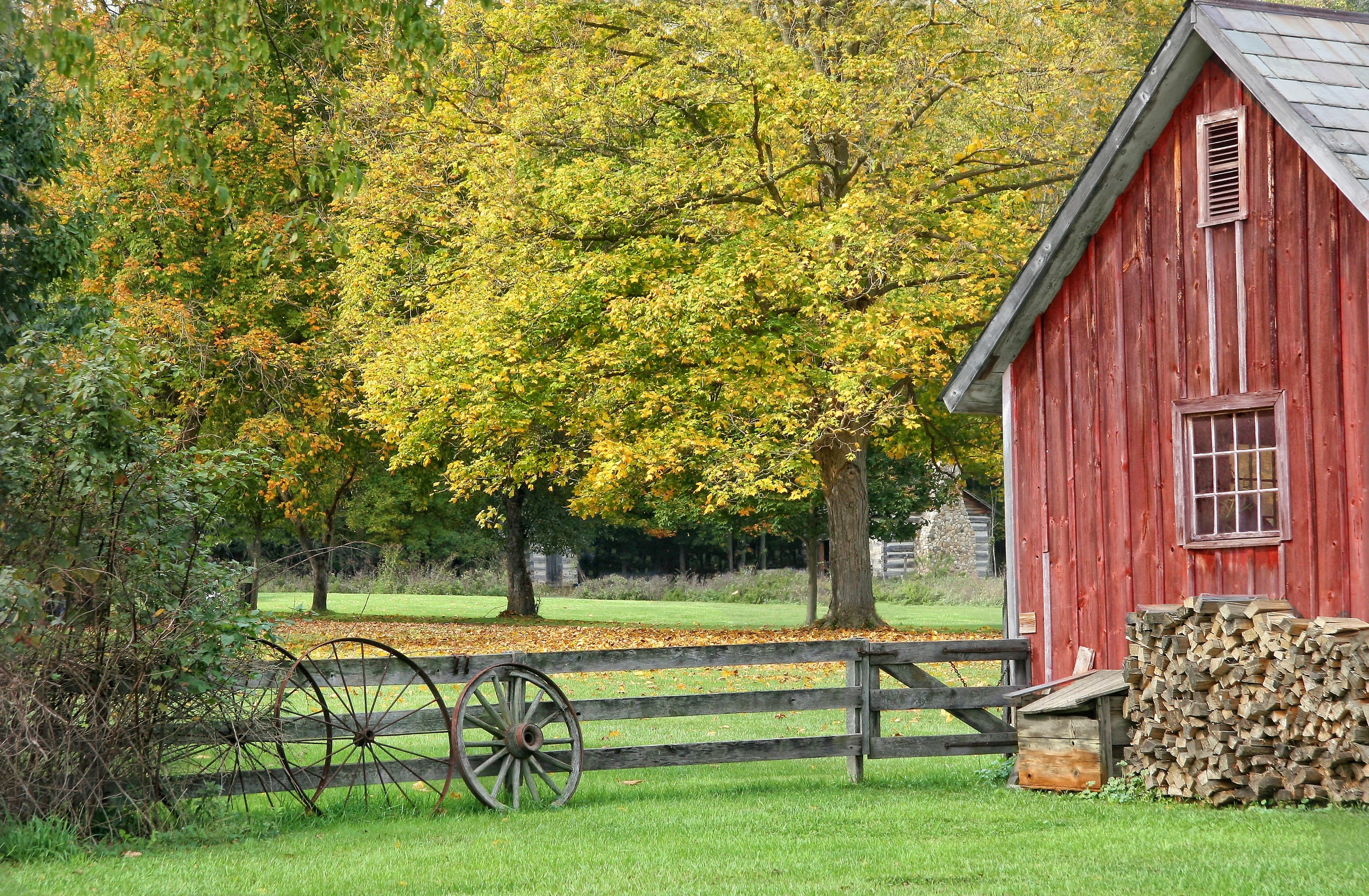 A red barn beside a wooden fence and autumn trees in a rural landscape.