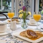 A beautifully set breakfast table with pancakes, coffee, orange juice, and fresh flowers.