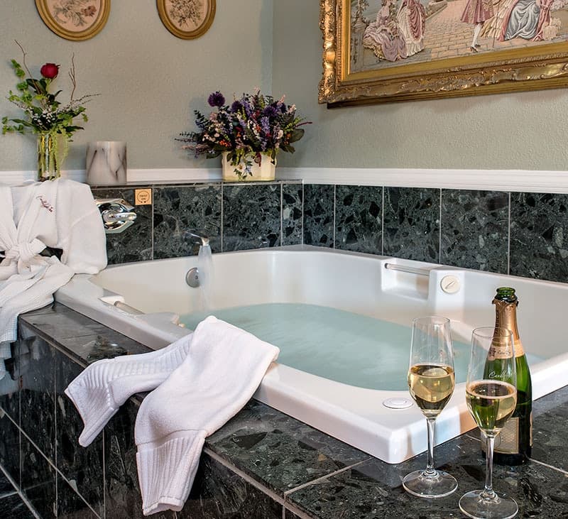 A luxurious bathroom featuring a jetted bathtub, plush towels, champagne flutes, and fresh flowers.