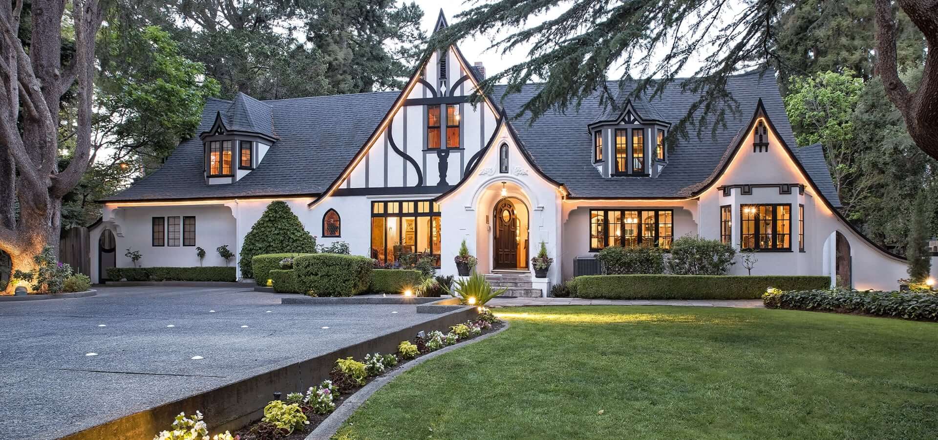 An elegant, Tudor-style house surrounded by lush greenery and well-maintained landscaping.