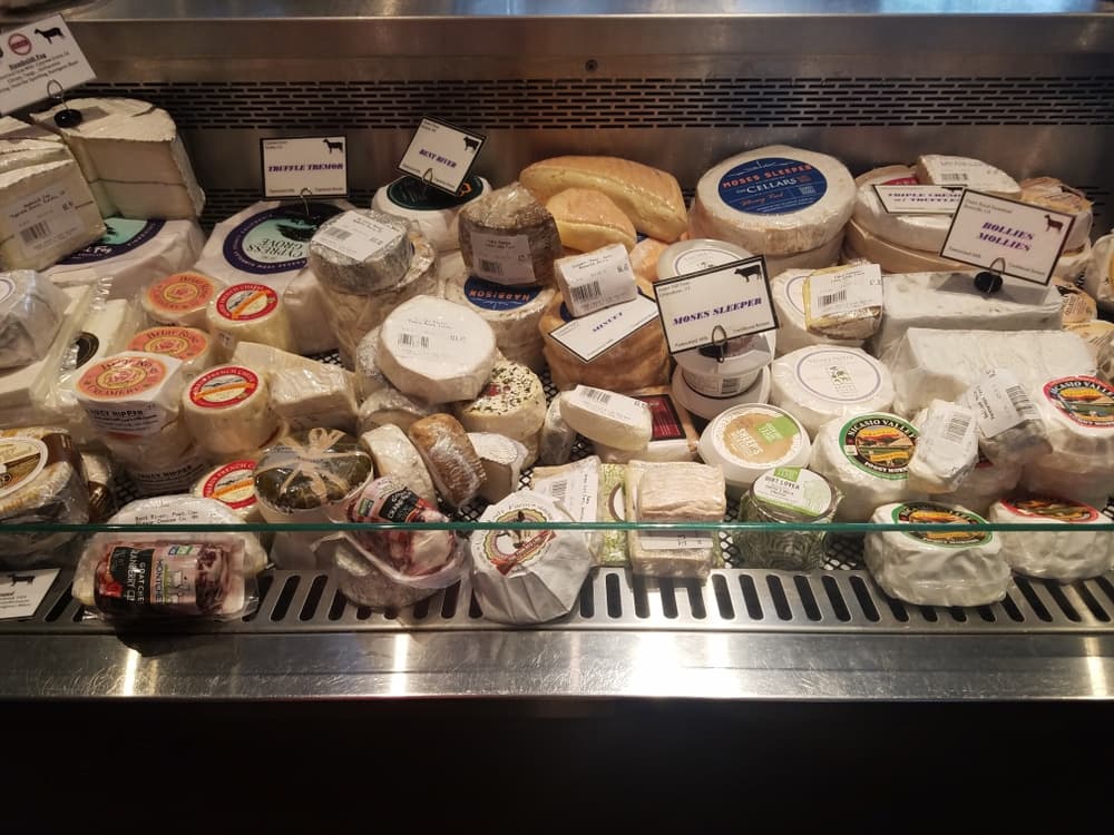 A display case filled with various types of cheese, each labeled with their names.