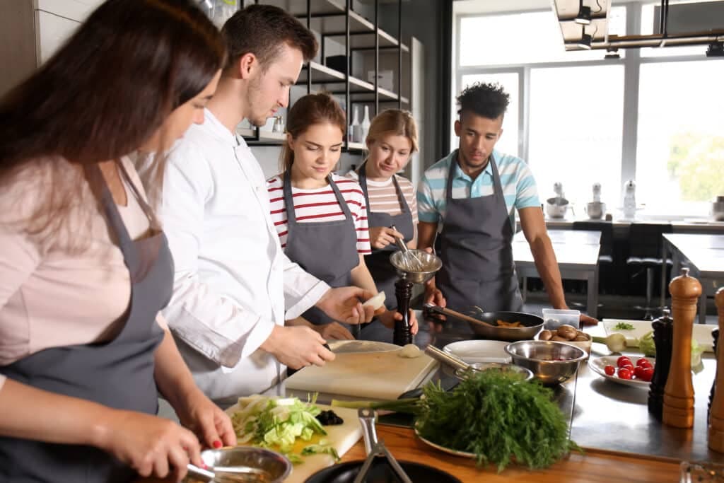 A group of five people in aprons is cooking together in a modern kitchen.