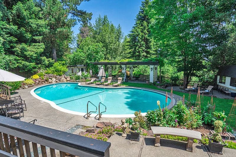 A serene backyard with a sparkling swimming pool surrounded by lush greenery and comfortable seating.