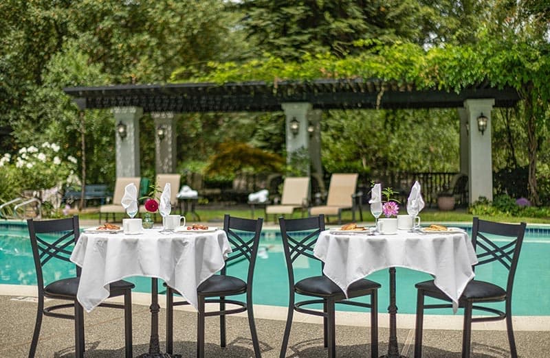Two elegantly set tables by a pool surrounded by lush greenery.
