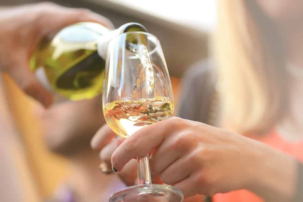 A hand pours white wine into a glass held by another hand.