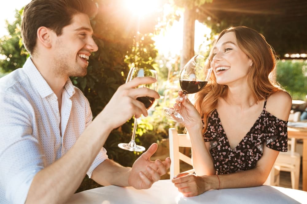A couple joyfully toasting with glasses of red wine outdoors.