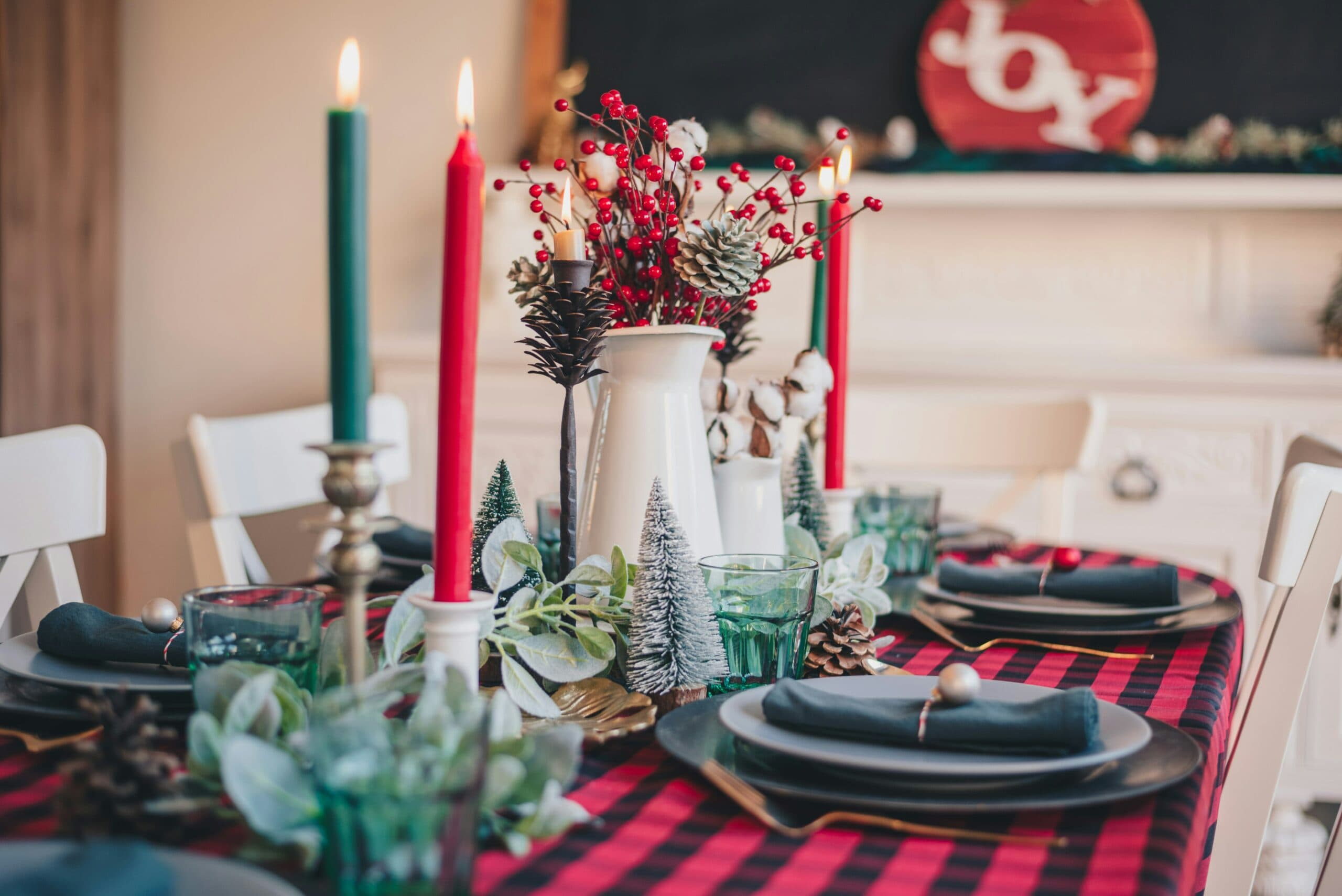 A festive dining table adorned with green and red candles, pinecones, and holiday decorations on a checkered tablecloth.