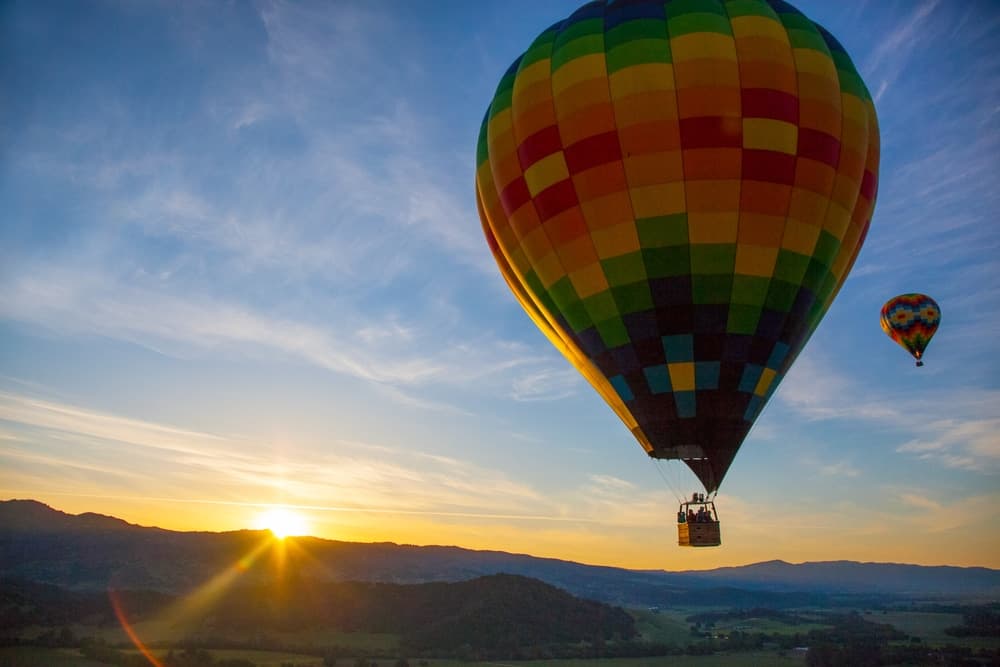 A colorful hot air balloon soars above a scenic landscape at sunrise.