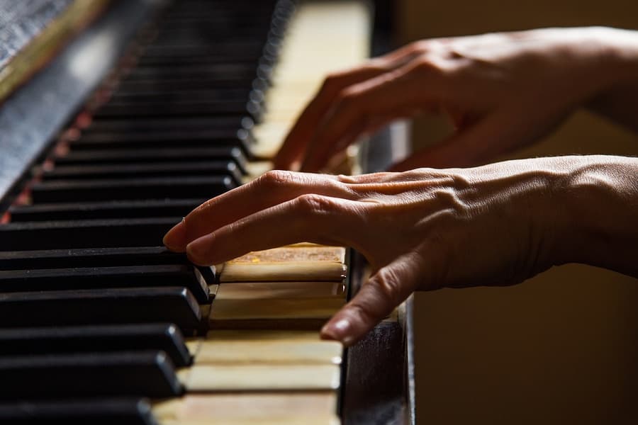 A close-up of hands playing an old piano.