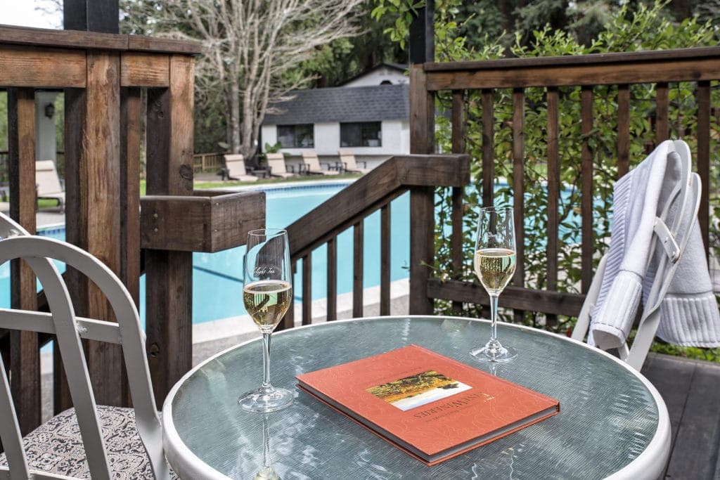 A cozy patio setting with two glasses of champagne, a menu, and a view of a swimming pool.