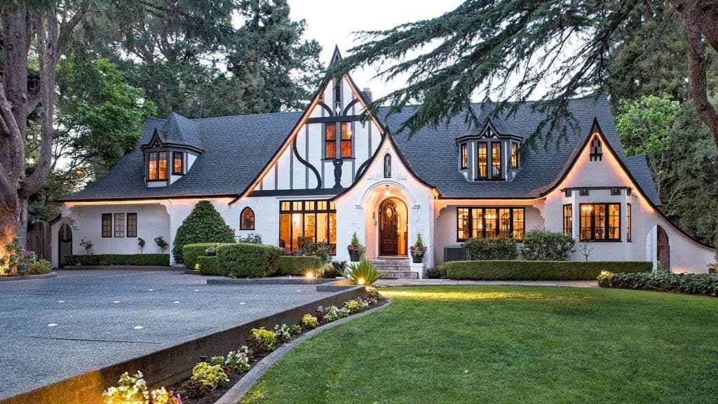 A charming Tudor-style house surrounded by lush landscaping and a spacious driveway.