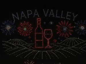 Colorful lights display the text "Napa Valley" above a wine bottle and glass, with fireworks in the background.