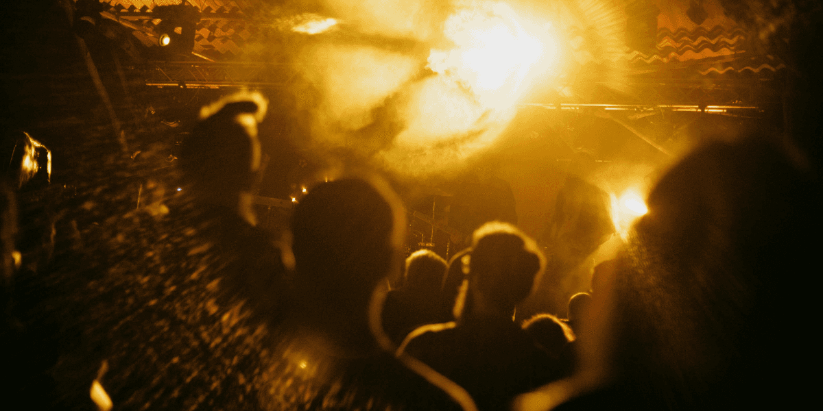 Silhouettes of a crowd enjoying a lively performance under bright, yellow stage lights.