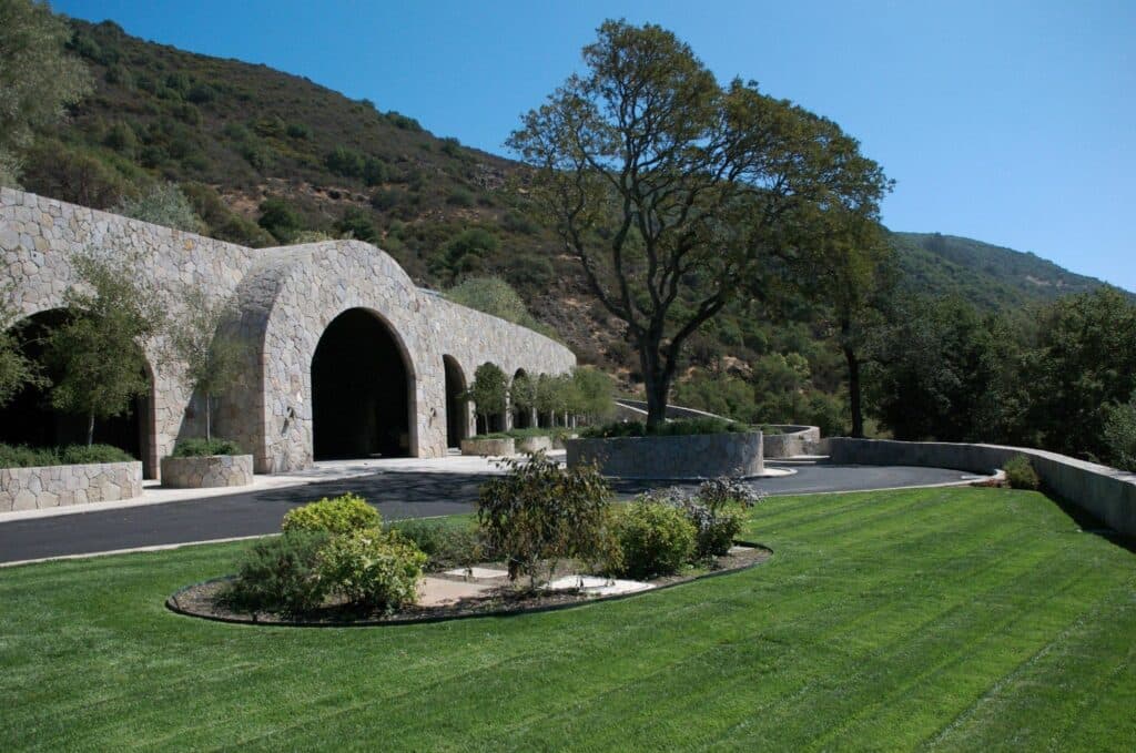 A modern stone building with archways set against a lush green landscape and rolling hills.