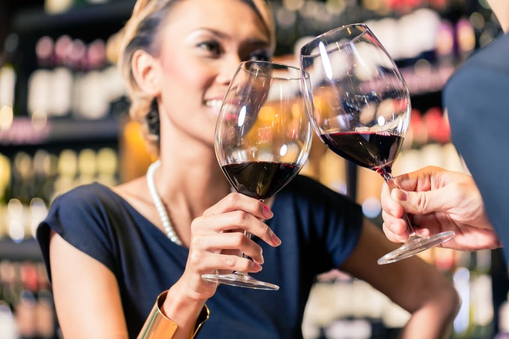 A woman smiles while clinking wine glasses with another person in a wine bar.