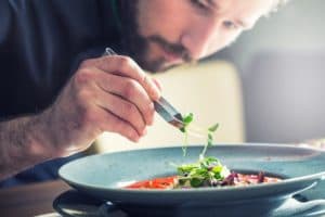 A chef meticulously garnishes a plate of food with fresh herbs.