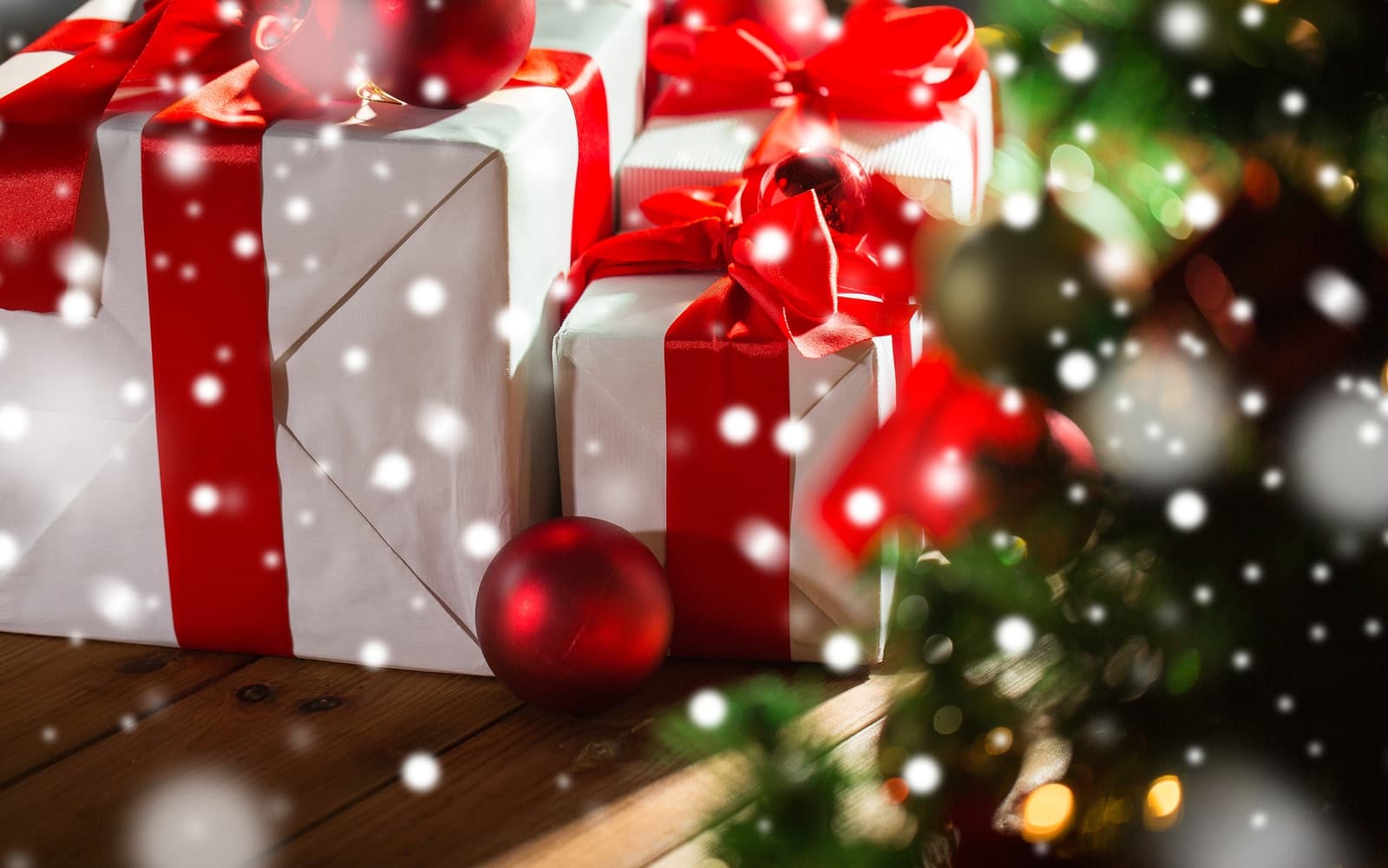 Christmas presents wrapped in white paper with red ribbons, surrounded by decorative ornaments and falling snow.